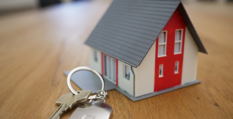 Clés accrochées à un porte-clés avec une maison et posées à côté d'une maison miniature sur une table en bois